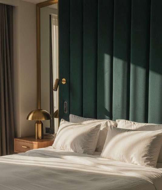 Room with a green velvet headboard and a brass lamp, in the afternoon light