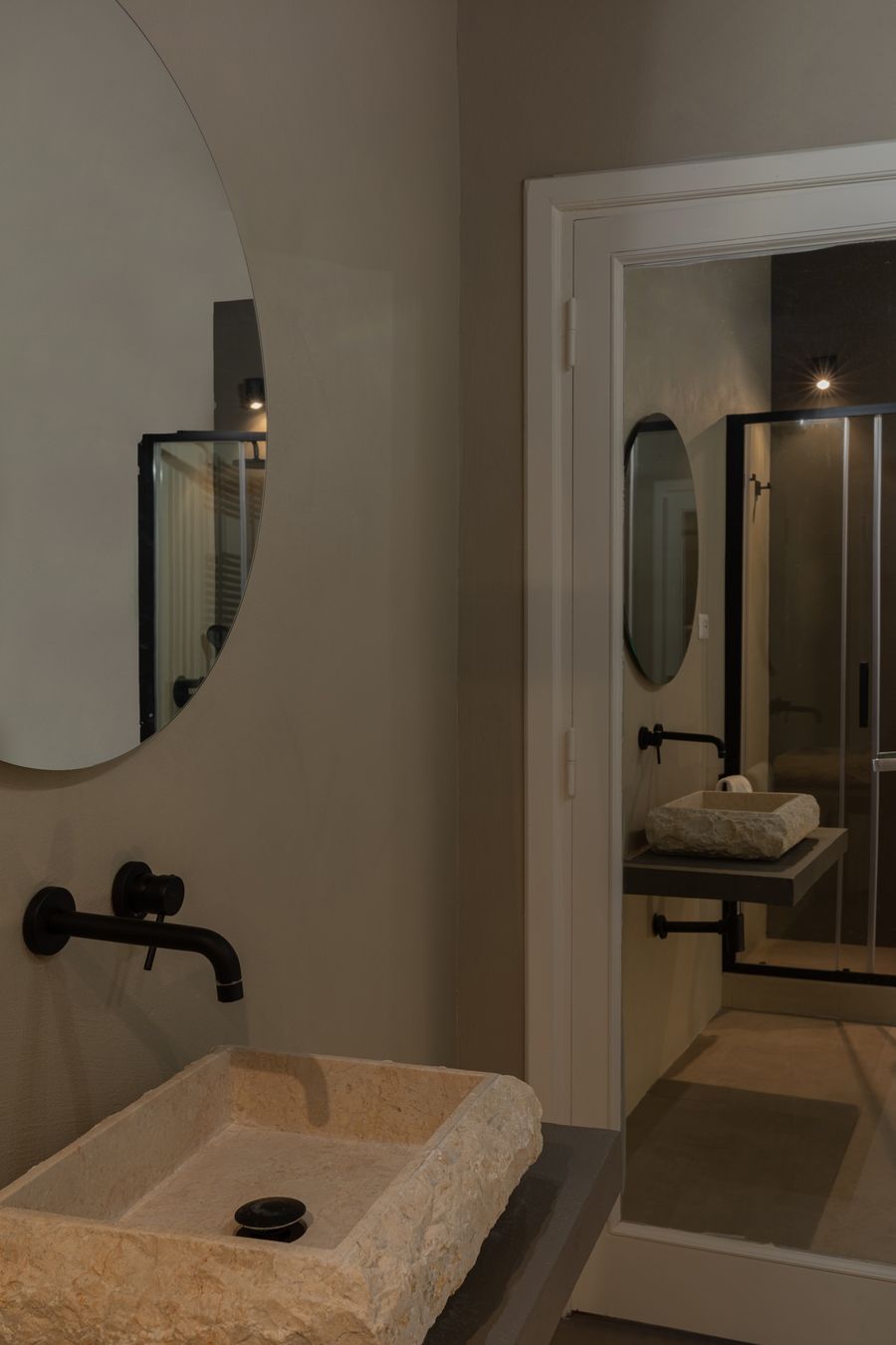Rough-hewn stone washbasin with black fittings and a round mirror